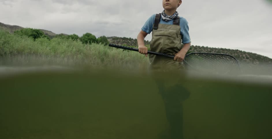A young boy wades through water carrying a fishing net