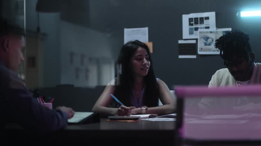 A woman talks and takes notes as she works with a team in an office