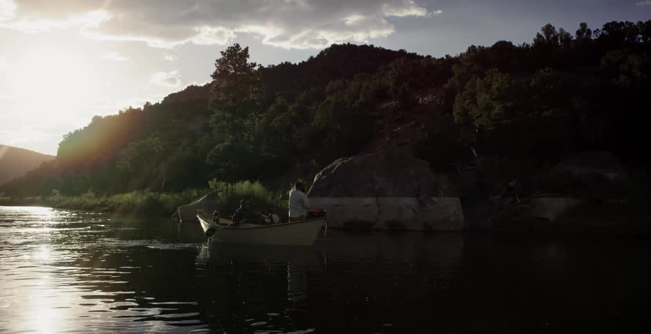 A man fishes on a river from his boat