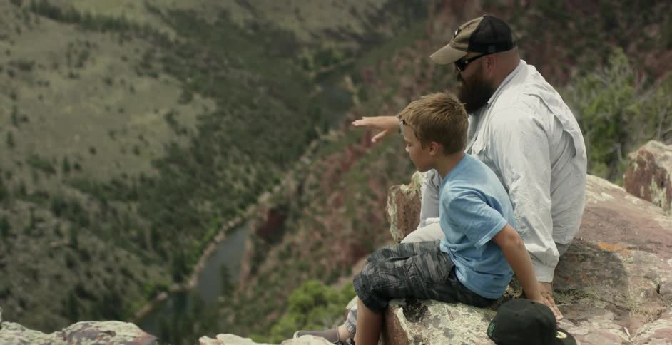 A man and a young boy sit at the top of a mountain
