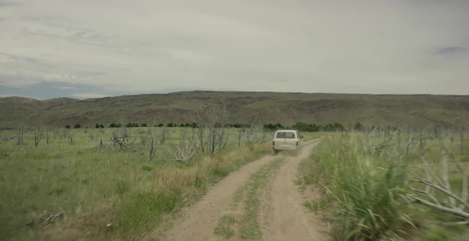 A vehicle travels down a dirt road in open land