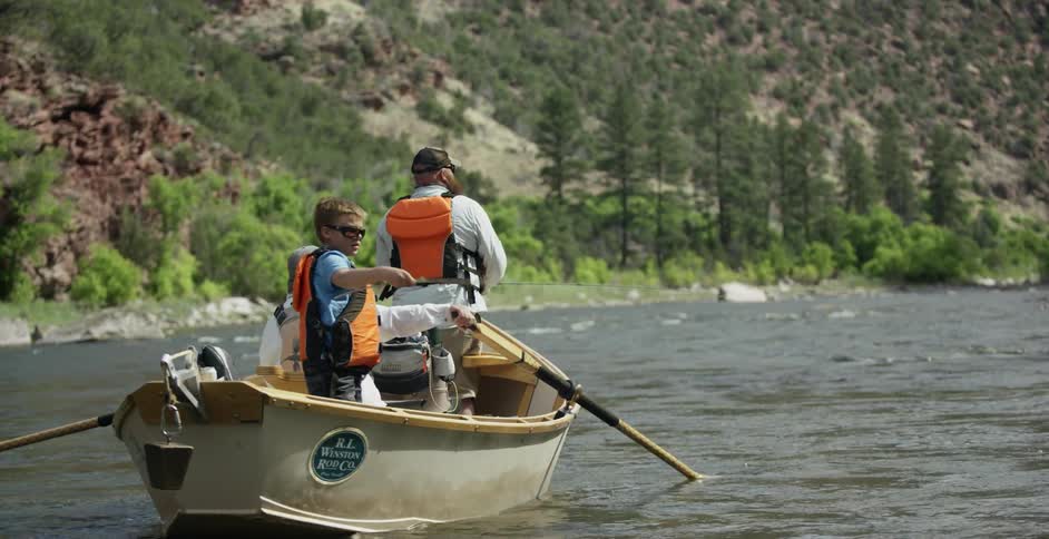 A man and boys are fishing in a row boat on a river during the day