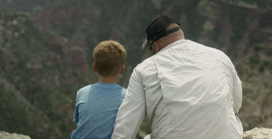 A man and a young boy are sitting on the edge of a cliff
