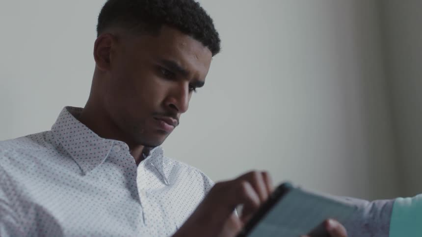 Man sits on a couch typing on a tablet