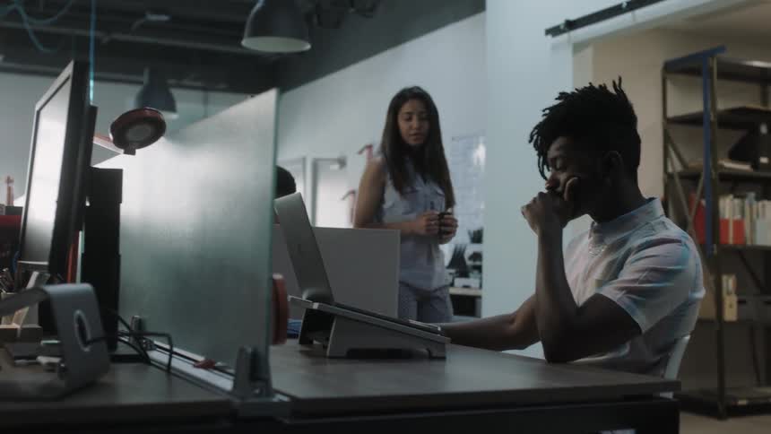 A woman approaches a man working in an office