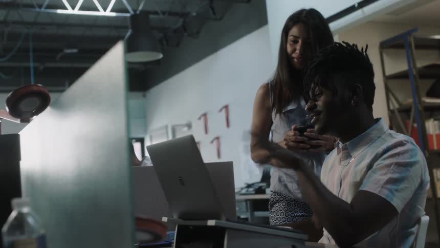 A man and woman in an office are discussing something on a computer
