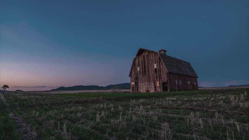 Timelapse of people walking in a field near an old barn
