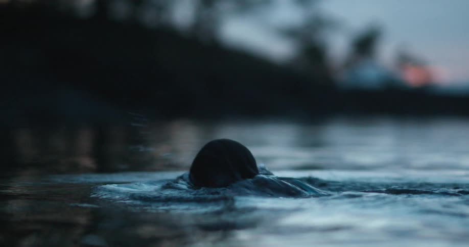 A woman swims in a lake at sunset