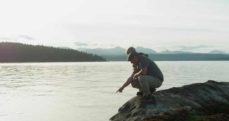 A father and son crouch next to a rippling lake