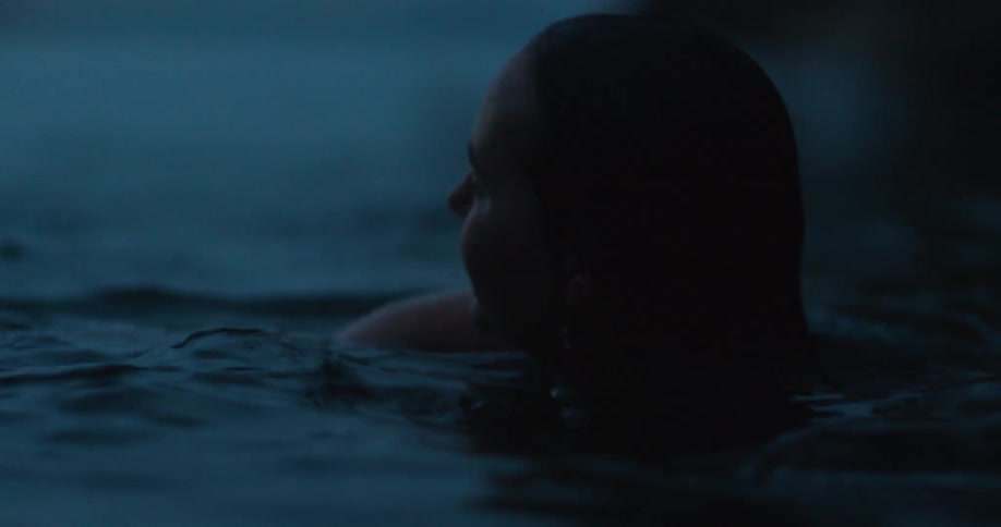 A woman swimming in a lake dunks below the water then surfaces