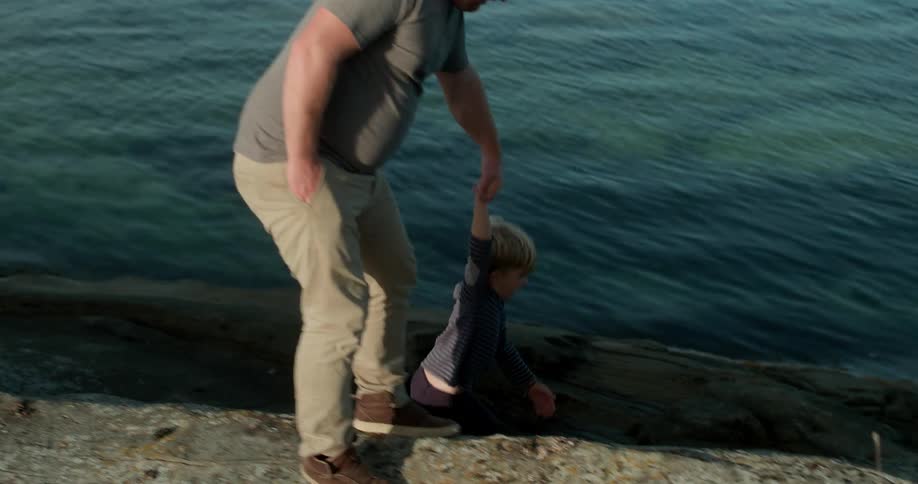 A father and son hold hands while walking on a lakeshore