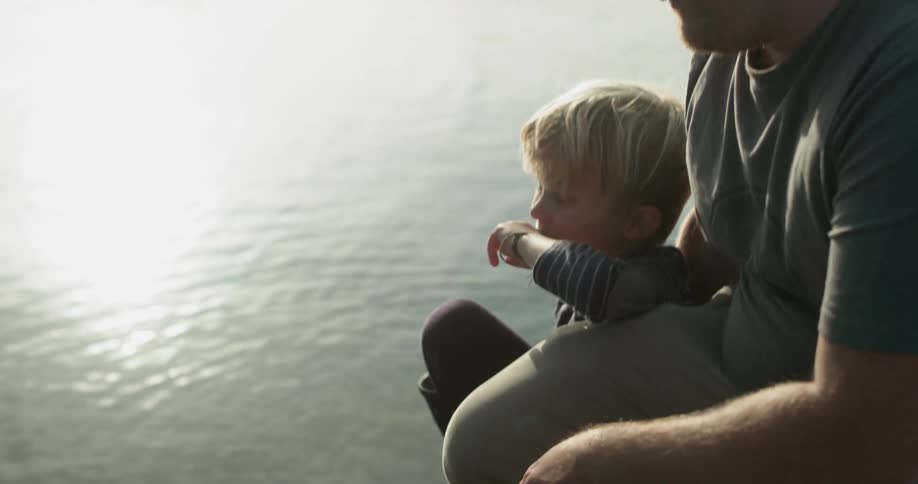 A father and son sit next to a rippling lake