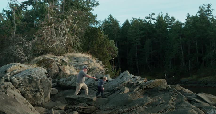 A man helps a young boy climb up rocks