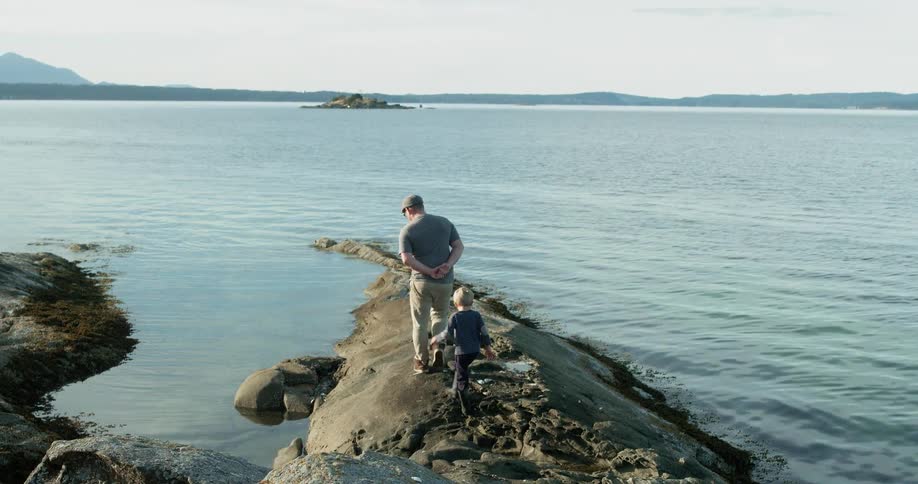 A father and son walk on a rock near the water