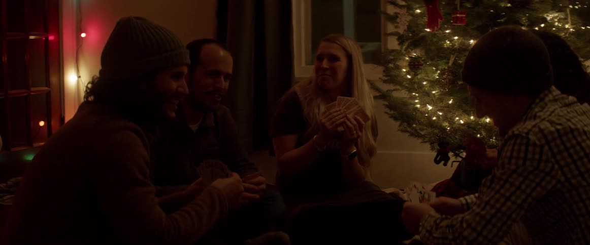 A group of people play cards by the christmas tree
