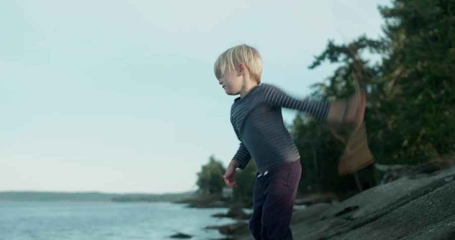 A young boy swings a stick and throws it into the water