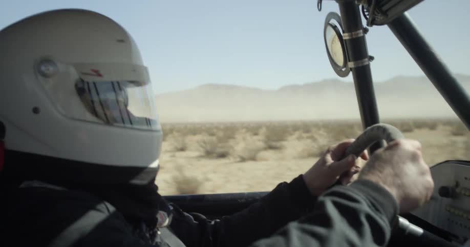 A driver wearing a helmet steer through the desert in a dune buggy