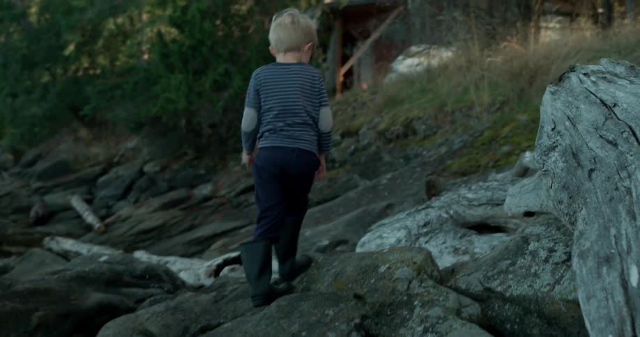 Child walks on a rocky shore near water