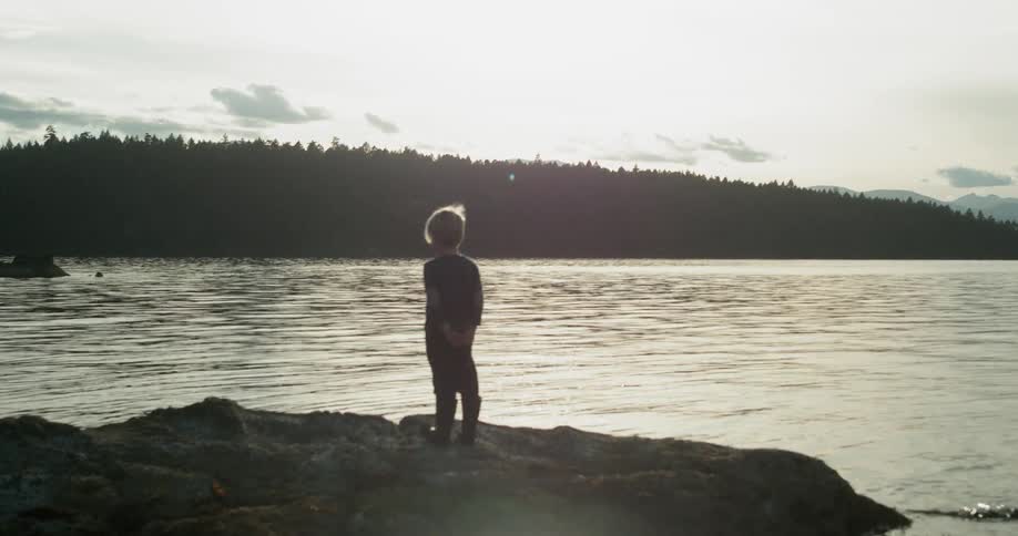 A person is standing near the water on rocks