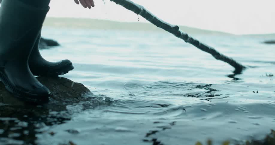 Person puts hand in water to grab a long stick