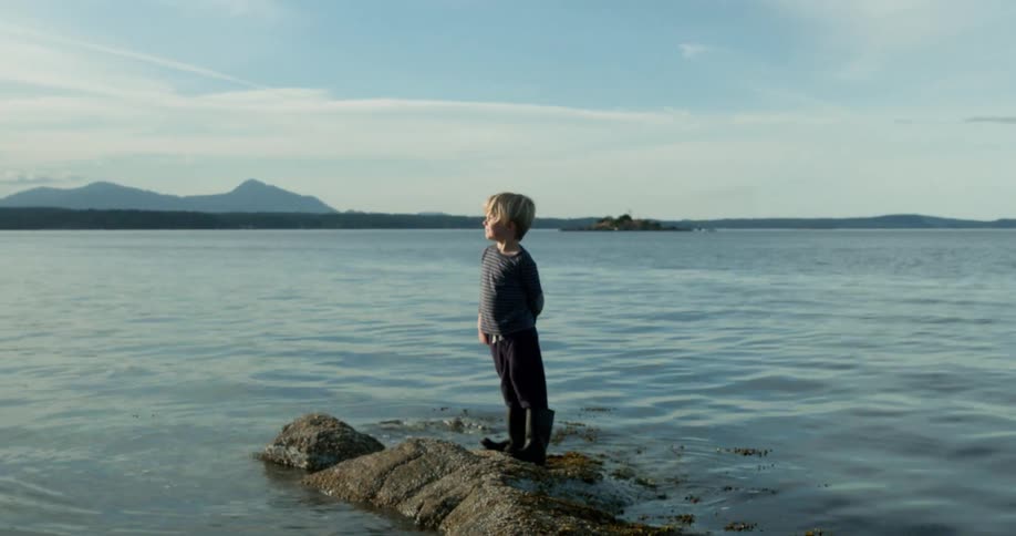 Young boy standing on a small rock formation that's extending into a large body of water