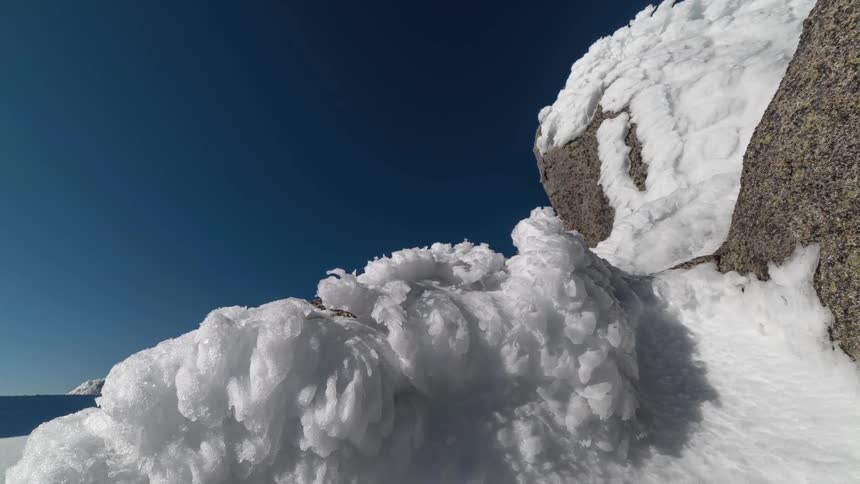 Piles of snow sits on the mountain under a blue sky