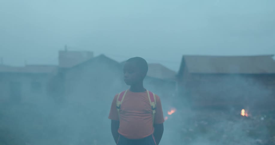 A child stands in a smoke filled courtyard with burning rubble