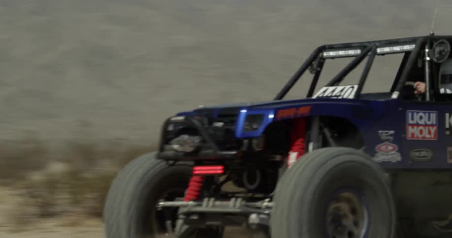 An off road vehicle drives in a desert while kicking up dust