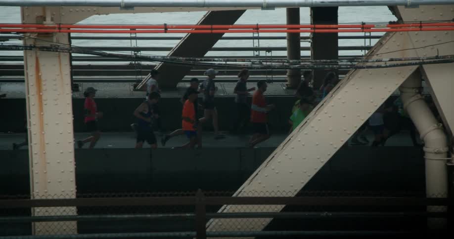 A group of marathon runners run across a bridge