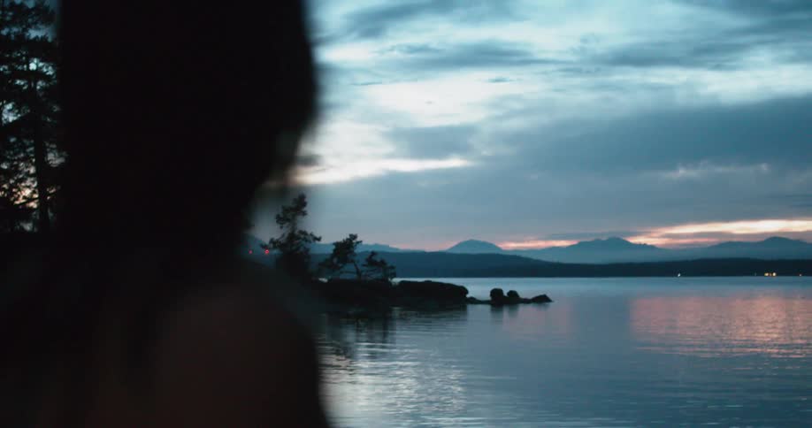 A woman stands on the shore near water