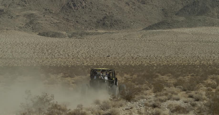 An off road vehicle drives  through a desert while kicking up dust