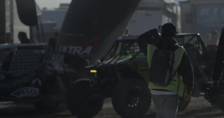People in yellow vests walking past a race car