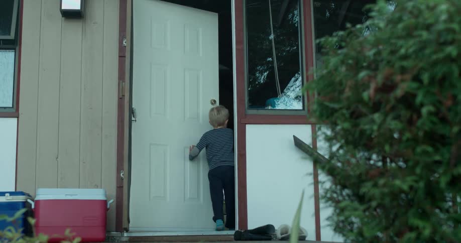 A young boy removes his shoes and enters a house