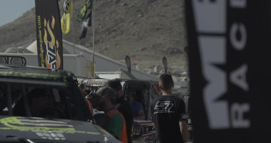 People are gathered around race cars outside on a sunny day