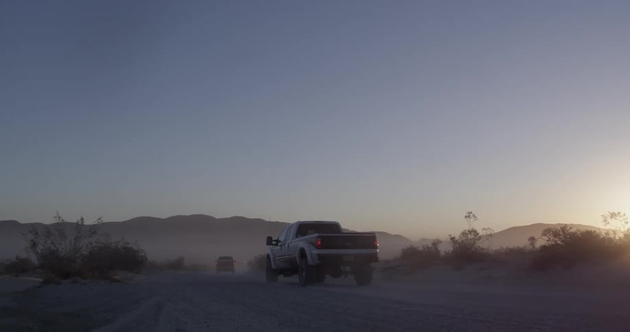 Trucks drive on a dirt road at sunset