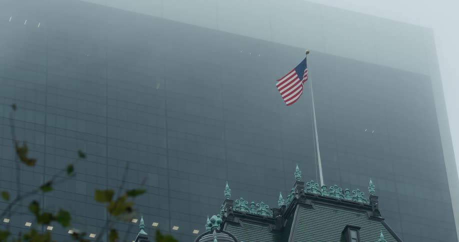 American flag waving in front of a large building on a hazy day