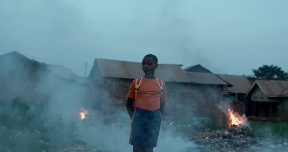 A young boy stands near huts as fires burn
