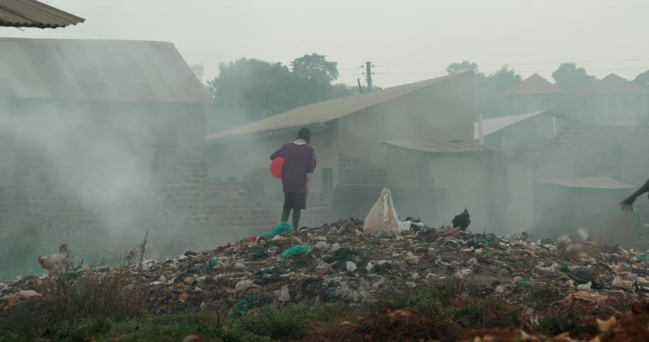 A boy stands on a pile of rubbish as smoke floats by