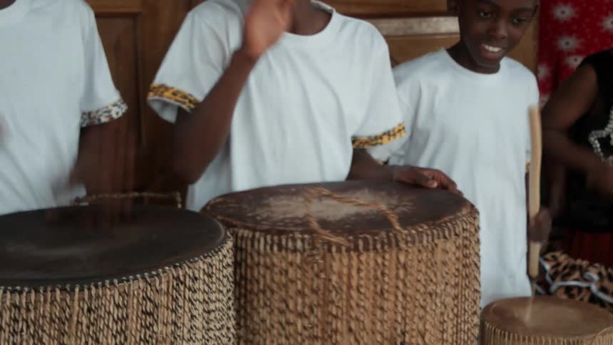 Three young men beating on drums using their hands and sticks