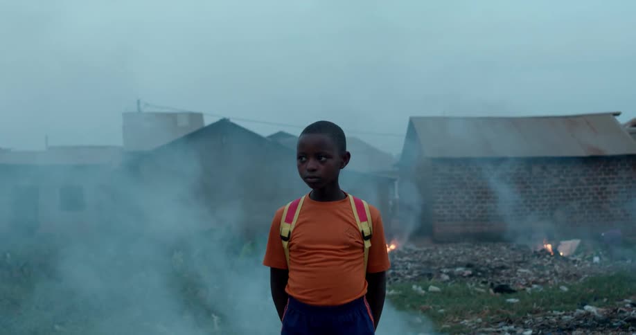 A young boy stands near huts as fires burn