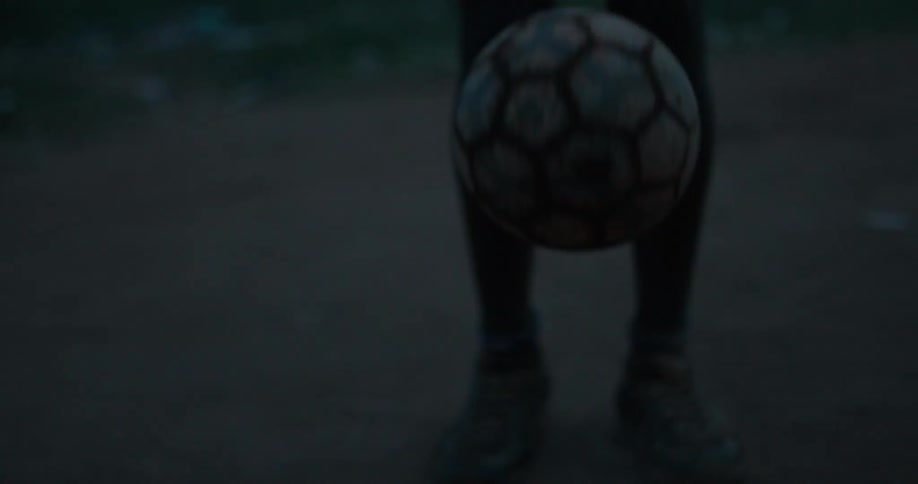 A boy bounces a soccer ball with his feet at dusk