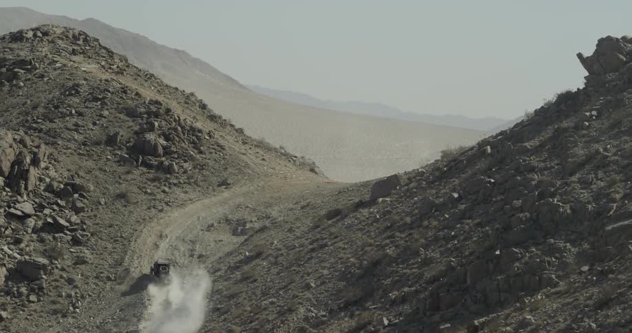A vehicle leaves a dust trail as it travels on a hilly dirt road