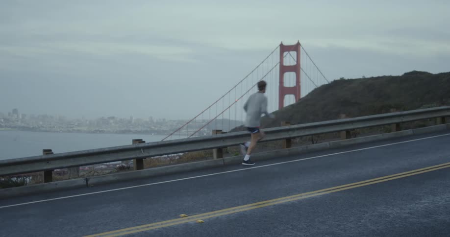 A man jogs on a road near a bridge