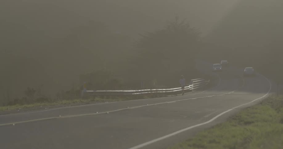 A person jogging on a country highway with cars going in both directions