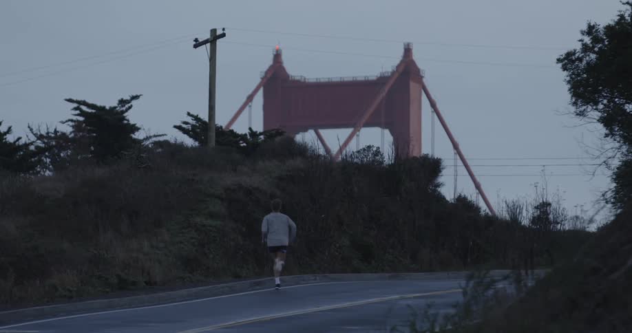 Man running down a road with a bridge on the side