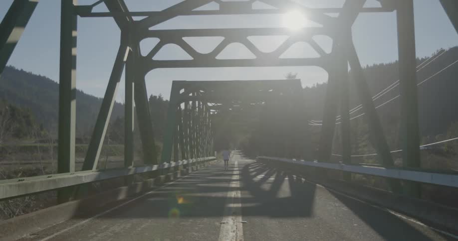 A jogger runs across a sunny rural bridge