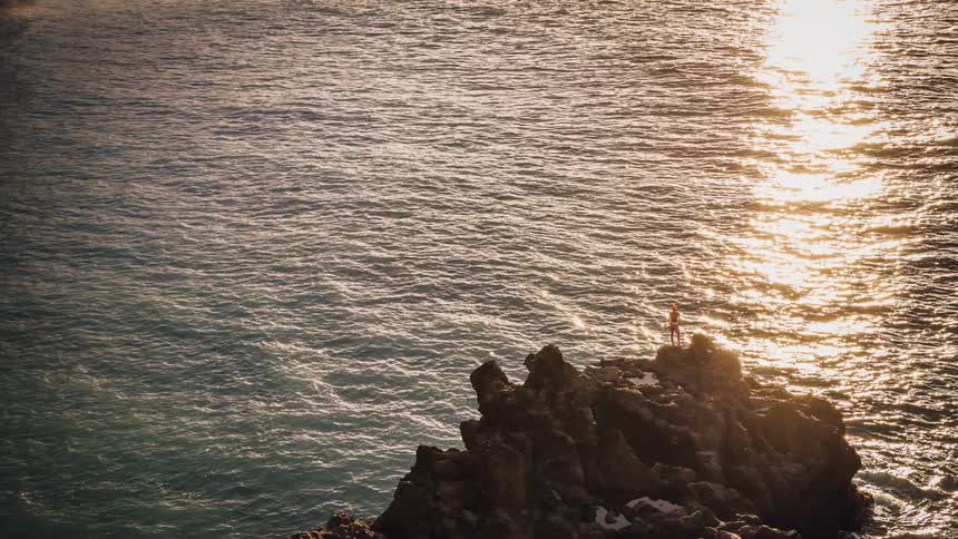 A person stands atop a rock formation in the water