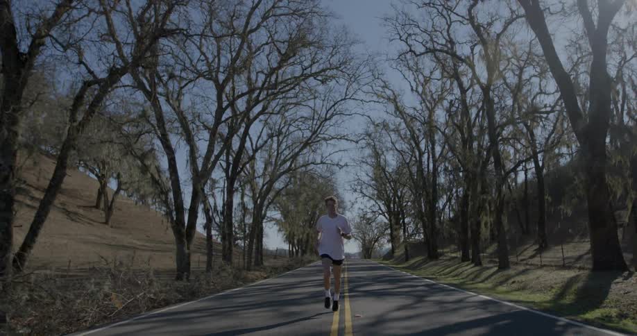 Man in white shirt jogs down the middle of the road
