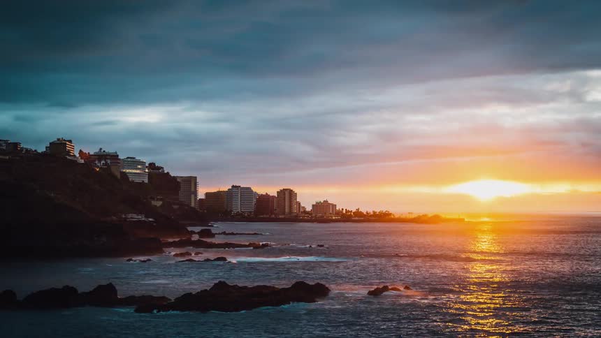 Storm clouds billow and roll near a coastal city from dawn to dusk