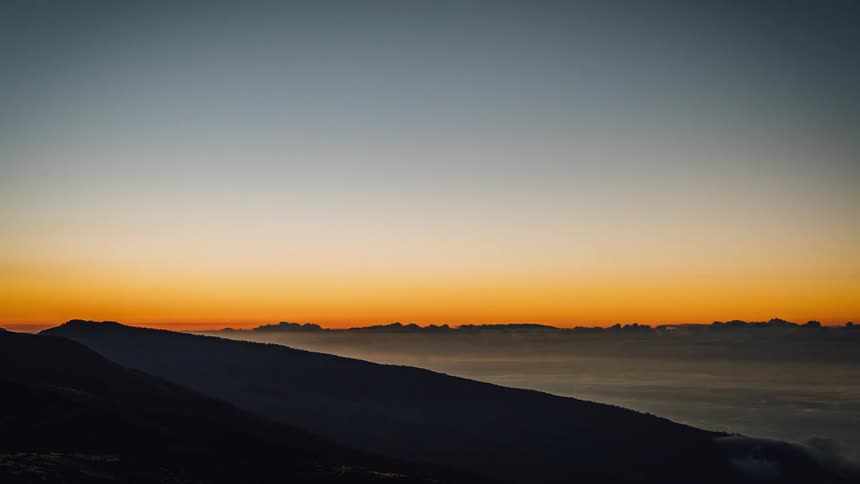 The sun sets behind foggy mountains